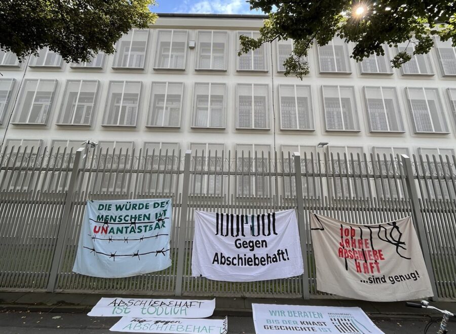 Bild einer Abschiebeeinrichtung mit Gittern vor den Fenstern. Davor hängen am Zaun zahlreiche Protestbanner