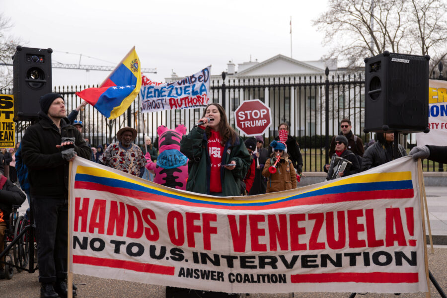 Protestierende nach dem US-Angriff auf Venezuela vor dem Weißen Haus. Eine Frau spricht ins Mikrofon, vor ihr ein Banner, auf dem Steht Hands off Venezuela (Hände weg von Venezuela).