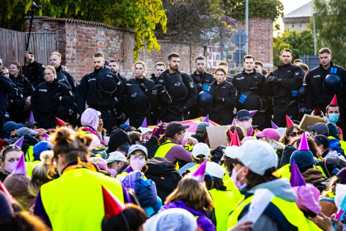 Man sieht demonstrierende Menschen, die auf dem Boden sitzen. Vor ihnen stehen viele Polizist*innen.
