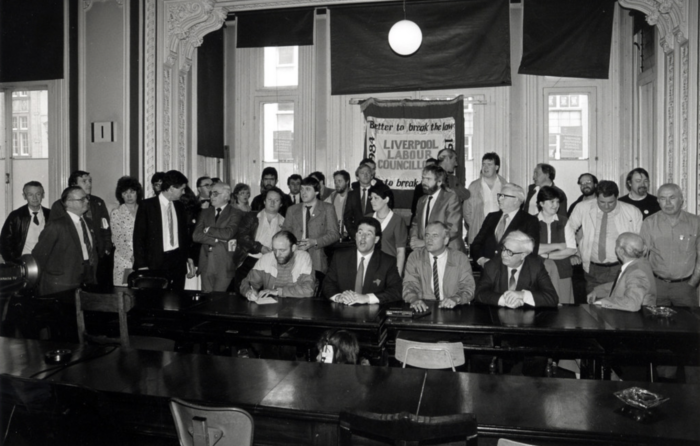 Man sieht auf einem Schwarzweißbild eine größere Menschengruppe in einem Saal, hinter ihnen hängt ein Transparent, auf dem steht Liverpool Labour Council.