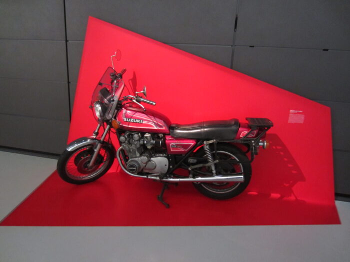 Vor rotem Hintergrund steht in einem Museum ein Motorrad der Firma Suzuki.