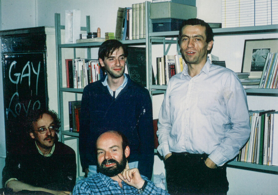 Die vier »Gründermütter« des Schwulen Museums Manfred Baumgart, Wolfgang Theis, Andreas Sternweiler und Manfred Herzer-Wigglesworth stehen in den Räumlichkeiten der AHA vor einem Bücherregal. Hinter ihnen ein Schrank, auf dem "Gay Love" gesprayt ist.