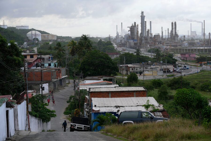 Im Vordergrund ist ein Wohngebiet und Palmen zu sehen, im Hintergrund die Türme einer Raffinerie.