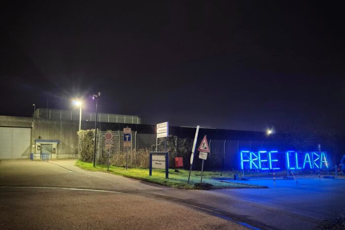 Einfahrt zur JVA Billwerder bei Nacht, auf der rechten Seite prangt in Neonröhren ein Free Clara Schriftzug