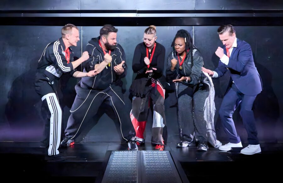 Fünf Schauspieler*innen auf einer dunklen Bühne, die Stein, Schere, Papier spielen