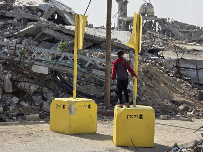 Vor einem Trümmerfeld zwei gelbe Klötze mit Stangen. Auf einem Klotz steht eine Person,