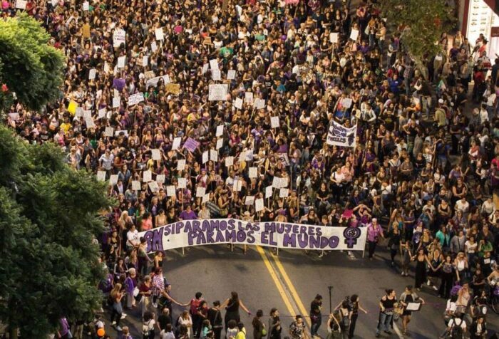 Bild von einer Demo zum 8. März 2018 in Uruguay. Menschen sind hinter einem Banner mit der Aufschrift "8M - Si paramos Las Mujeres - Paramos El Mundo" (dt. Wenn Frauen stoppen, steht die Welt still) versammelt.