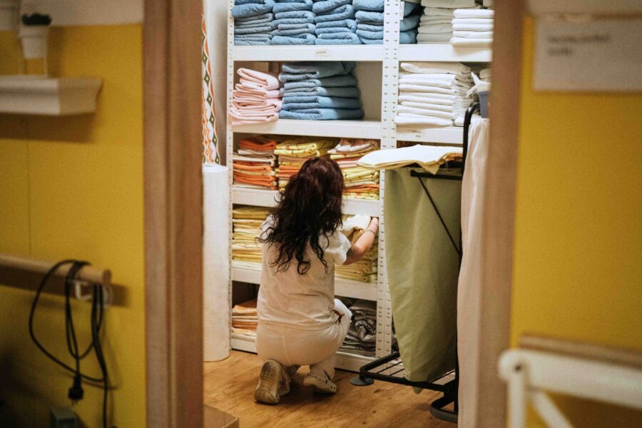 Eine Frau in weißer Krankenhauskleidung sortiert Bettbezüge in einen Schrank