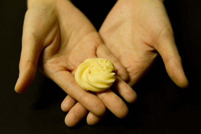 Das Bild zeigt einen Kringel Butter in der den Händen einer Person vor schwarzem Hintergrund