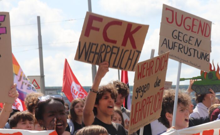 Schulstreik am 8. Mai in Frankfurt. Schüler*innen stehen hinter einem Banner und halten Schilder hoch, unter anderem mit den Slogans "Jugend gegen Aufrüstung" und "Wehr dich gegen die Wehrpflicht".