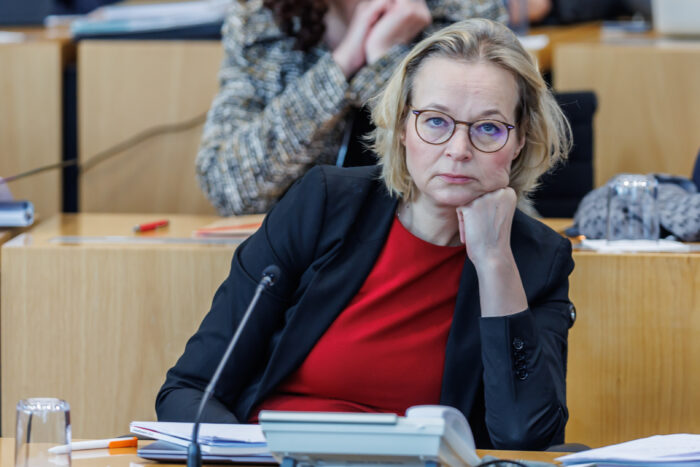Man sieht eine Frau, Katja Wolf, die mit einem müden Gesichtsausdruck den Kopf auf ihre Faust gestützt hat.