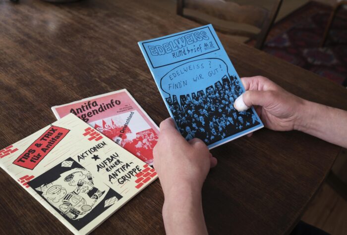 Auf einem Tisch liegen zeei alte Antifa-Hefte, in der Hand hält jemand ein weiteres mit dem Titel "Edelweiß Rundbrief Nr. 2"