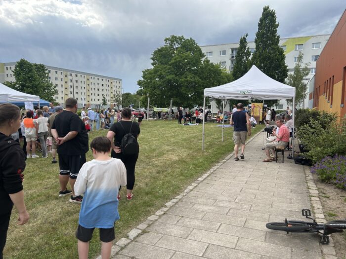 Man sieht Leute auf einer Wiese vor einem Neubaugebiet.
