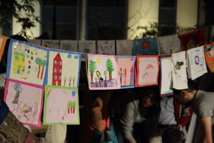 Wahrscheinlich von Kindern gemalte Bilder hängen über dem Taksim-Platz, darunter sitzen Menschen im Kreis.