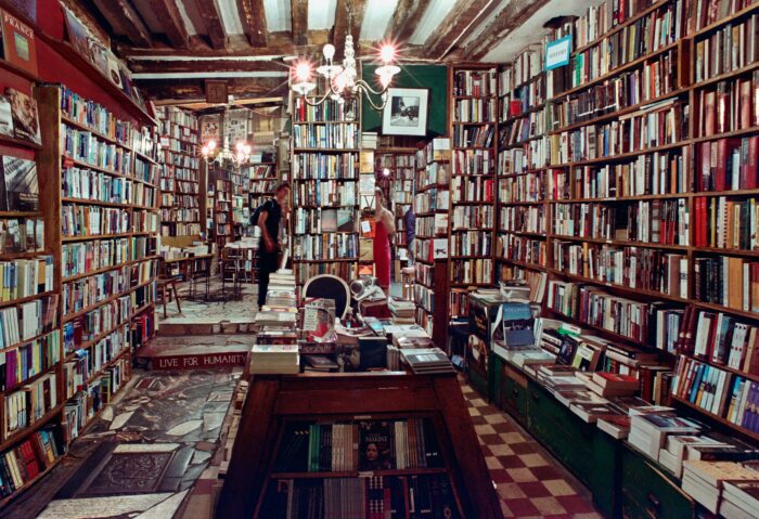 Das Bild zeigt einen Buchladen. Die Regale reichen bis unter die Decke und sind vollgestellt mit Büchern