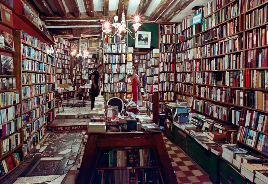 Das Bild zeigt einen Buchladen. Die Regale reichen bis unter die Decke und sind vollgestellt mit Büchern