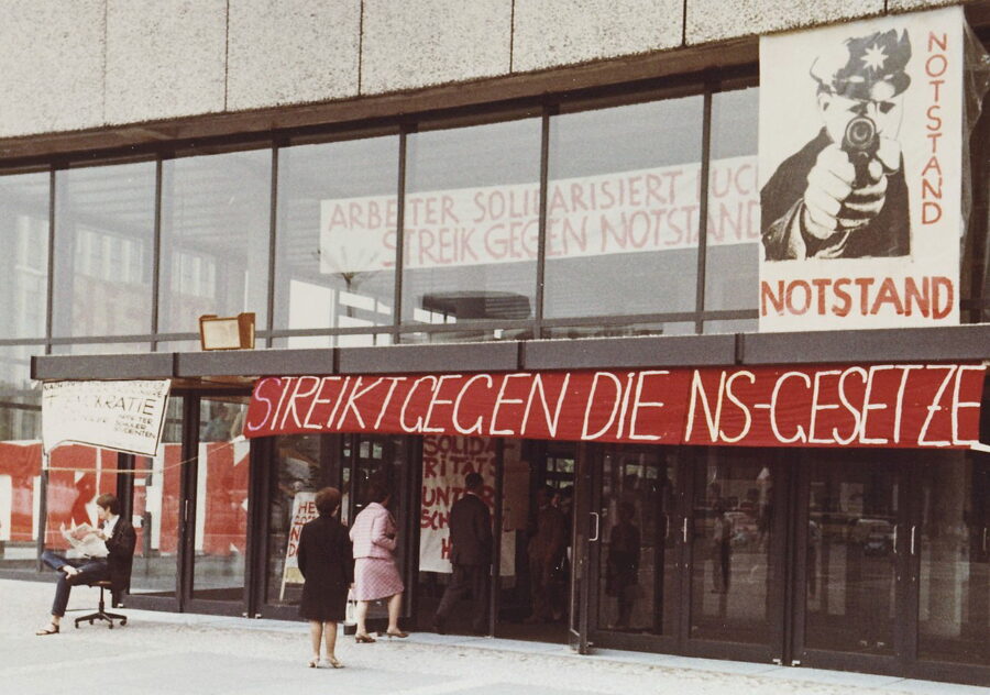 Eingang einer Universität, darüber ein Transparent in rot, mit der Aufschrift "streikt gegen die NS-Gesetze"