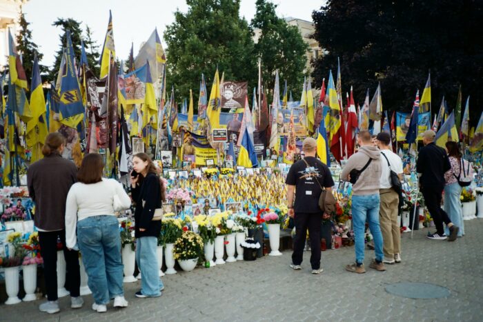 Man sieht ein Meer aus Blumen und Fahnen, einige Menschen davor.