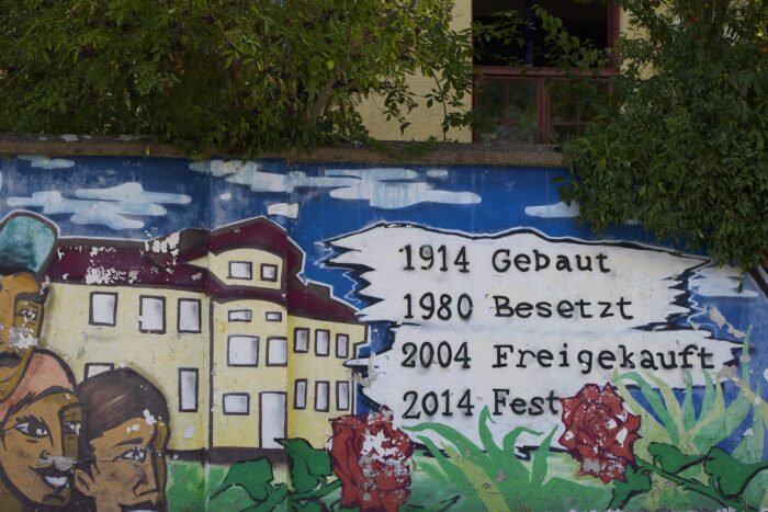 Man sieht eine Mauer mit Graffiti auf dem steht 1914 gebaut 1980 besetzt 2004 freigekauft