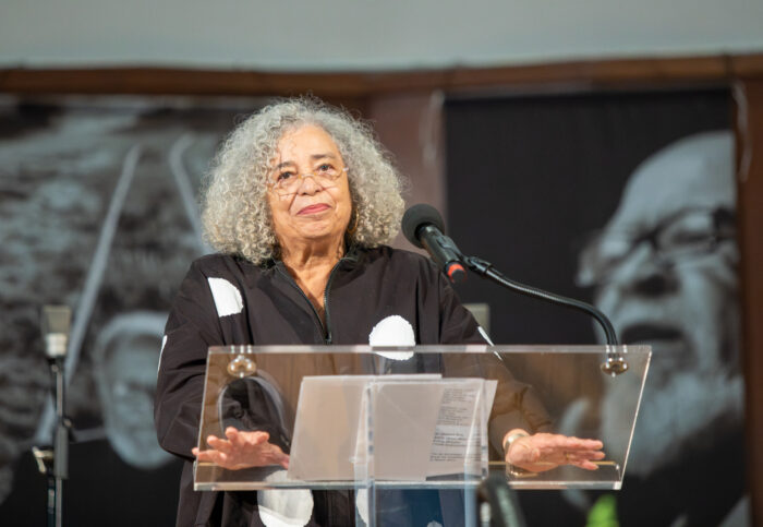 Man sieht Angela Davis an einem Rednerpult stehen.
