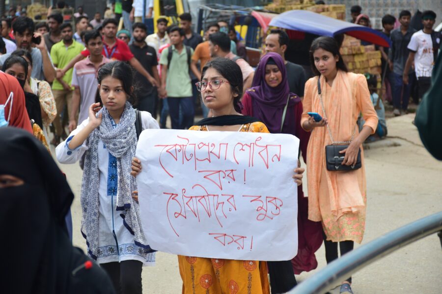 Eine Frau hält bei den Protesten 2024 in Bangladesch ein Schild hoch, das zur Reformierung des Quotengesetzes aufruft.