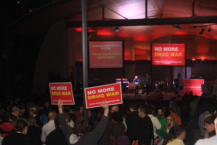 Das Foto zeigt eine Protestveranstaltung in Los Angeles 2011. Menschen halten Schilder mit der Aufschrift No More Drugs War in die Höhe. Es ist Abend