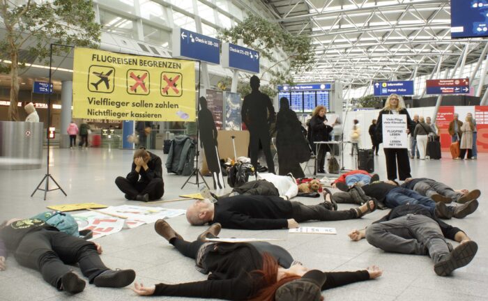Ein paar Menschen liegen wie tot auf dem Fußboden einer Halle. Protestplakate.